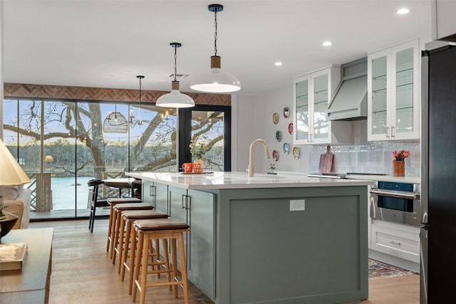 kitchen featuring pendant lighting, custom exhaust hood, stainless steel appliances, tasteful backsplash, and a center island with sink