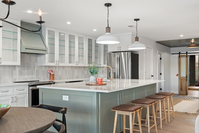 kitchen with stainless steel appliances, an island with sink, white cabinets, a barn door, and light wood-type flooring