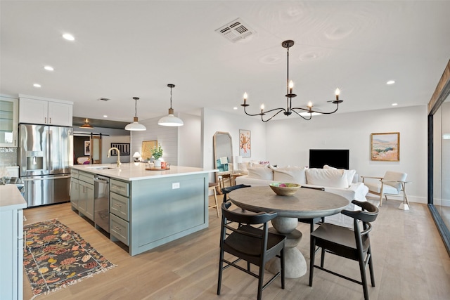 kitchen featuring decorative light fixtures, light hardwood / wood-style flooring, stainless steel appliances, and a center island with sink