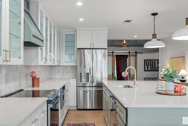 kitchen with pendant lighting, sink, white cabinetry, stainless steel appliances, and a barn door