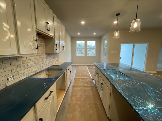 kitchen featuring white cabinetry, dark stone countertops, cooktop, backsplash, and hanging light fixtures