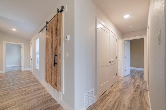 hallway with a barn door, light hardwood / wood-style floors, and vaulted ceiling