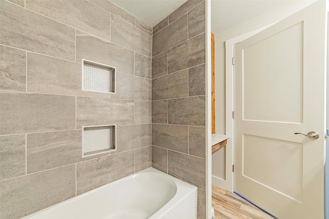 bathroom with a textured ceiling, wood-type flooring, and tiled shower / bath combo