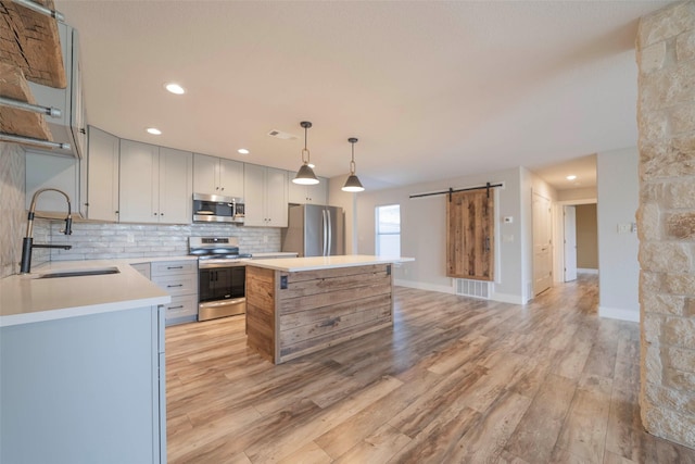 kitchen with sink, stainless steel appliances, a barn door, decorative light fixtures, and a kitchen island