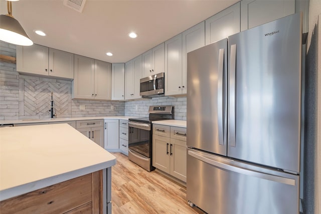 kitchen with sink, decorative light fixtures, decorative backsplash, appliances with stainless steel finishes, and light wood-type flooring