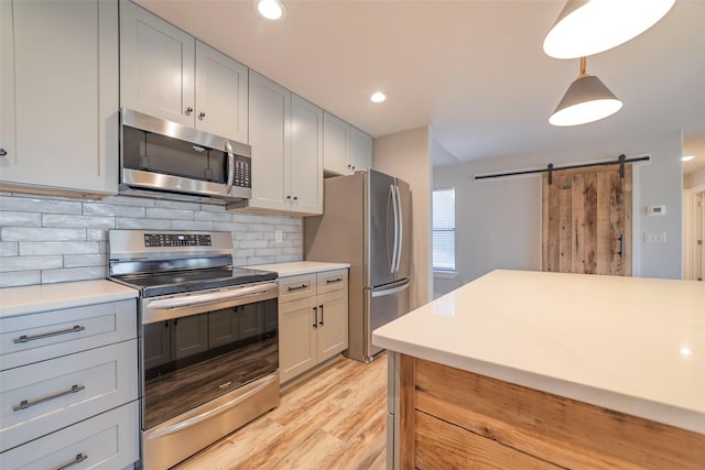 kitchen with stainless steel appliances, tasteful backsplash, a barn door, light hardwood / wood-style flooring, and pendant lighting