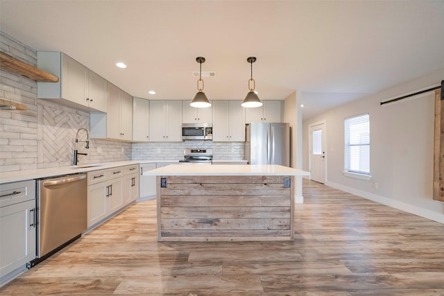 kitchen featuring sink, a barn door, decorative light fixtures, a kitchen island, and stainless steel appliances