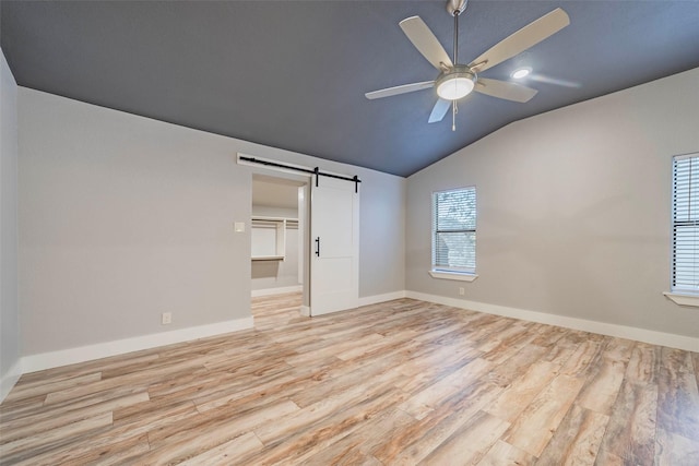 unfurnished bedroom with a walk in closet, ceiling fan, a barn door, light hardwood / wood-style flooring, and lofted ceiling