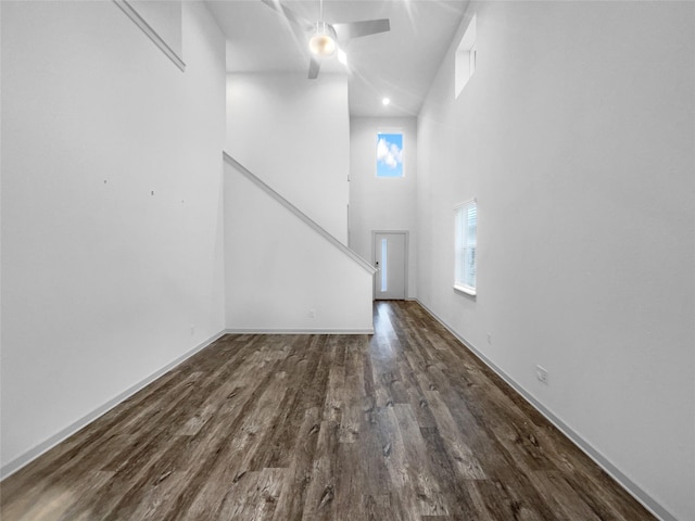 unfurnished living room with ceiling fan, a towering ceiling, and dark wood-type flooring