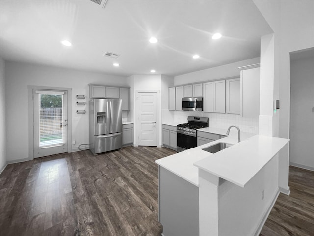 kitchen with dark wood-type flooring, sink, decorative backsplash, appliances with stainless steel finishes, and kitchen peninsula