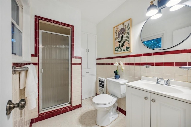 bathroom with toilet, heating unit, tile walls, vanity, and a shower with door