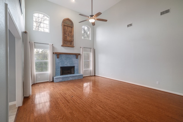 unfurnished living room featuring ceiling fan, a towering ceiling, a fireplace, and a wealth of natural light