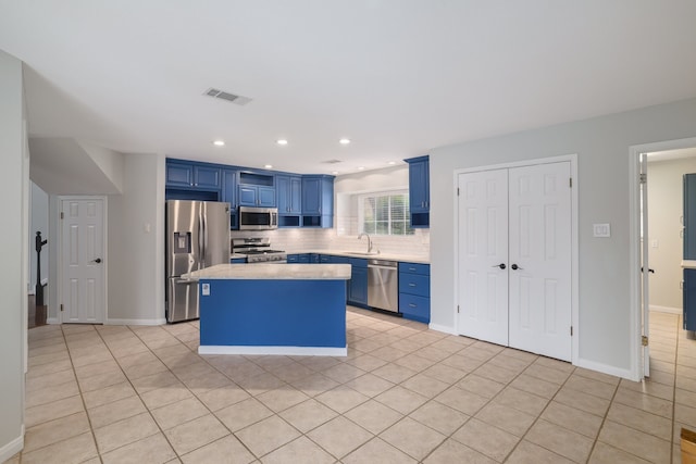 kitchen with appliances with stainless steel finishes, blue cabinets, sink, light tile patterned floors, and a kitchen island