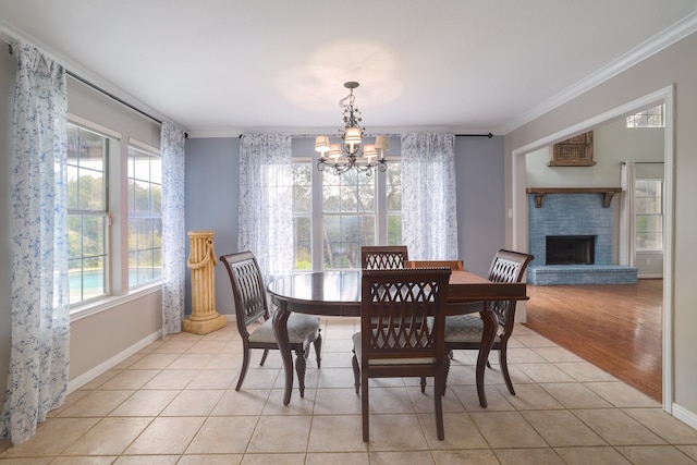 tiled dining room with a chandelier, a brick fireplace, and crown molding