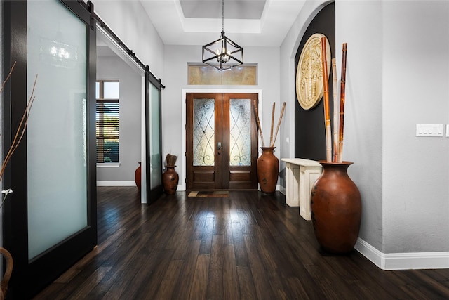 entryway featuring french doors, a tray ceiling, a barn door, a notable chandelier, and dark hardwood / wood-style floors