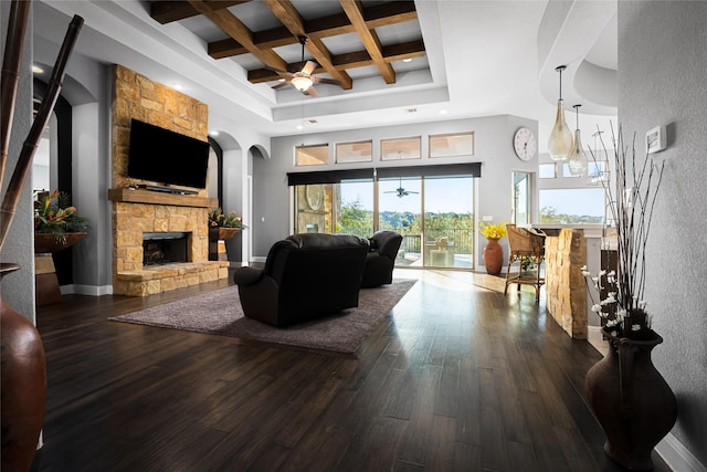 living room featuring beam ceiling, a high ceiling, coffered ceiling, a stone fireplace, and hardwood / wood-style flooring