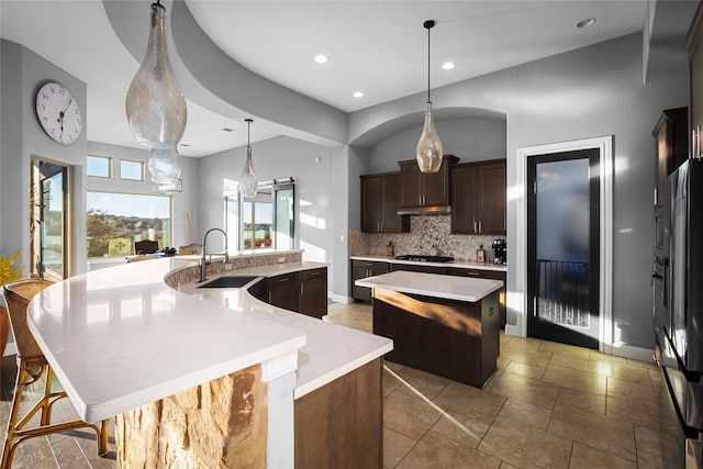 kitchen with dark brown cabinetry, sink, tasteful backsplash, pendant lighting, and a spacious island