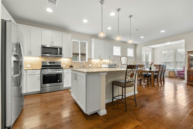 kitchen with white cabinets, a center island, stainless steel appliances, and hanging light fixtures