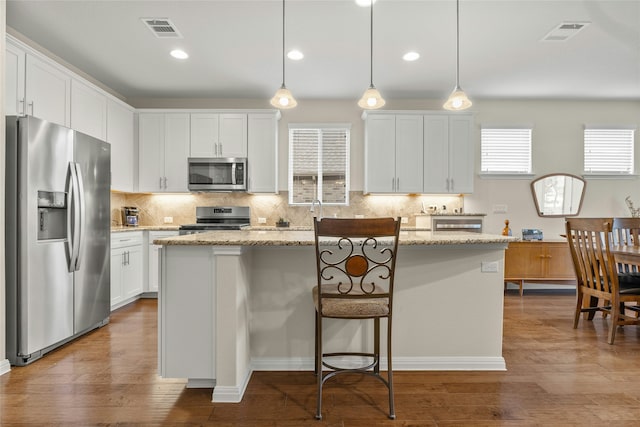 kitchen featuring white cabinets, decorative light fixtures, a center island, and appliances with stainless steel finishes