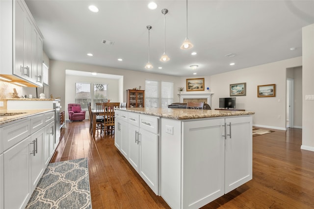 kitchen with dark hardwood / wood-style flooring, light stone counters, a kitchen island, decorative light fixtures, and white cabinetry