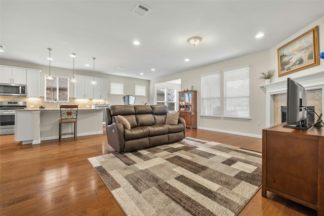 living room featuring a tiled fireplace, sink, and light hardwood / wood-style flooring