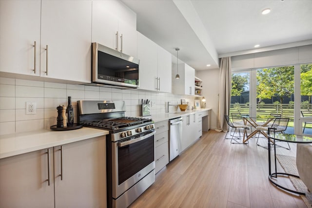 kitchen with decorative backsplash, stainless steel appliances, white cabinetry, and hanging light fixtures