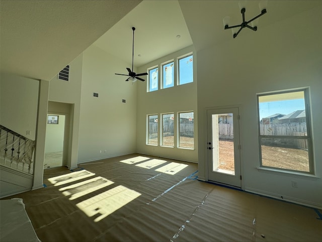 unfurnished living room featuring visible vents, ceiling fan, a towering ceiling, and baseboards