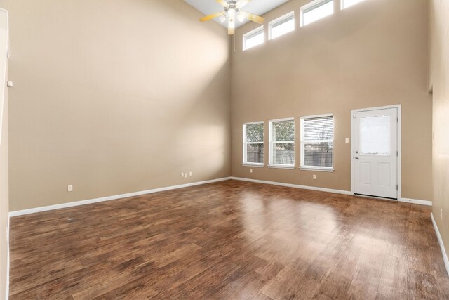 unfurnished living room with a towering ceiling, ceiling fan, and dark wood-type flooring