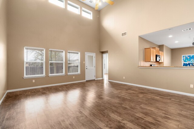 unfurnished living room with ceiling fan, dark wood-type flooring, and a high ceiling