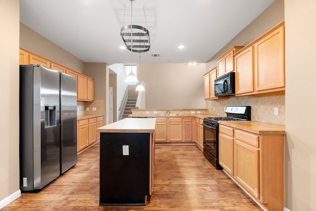 kitchen with black appliances, hanging light fixtures, light wood-type flooring, light brown cabinetry, and a kitchen island