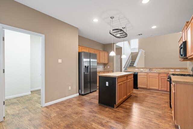 kitchen with light brown cabinetry, backsplash, sink, black appliances, and decorative light fixtures