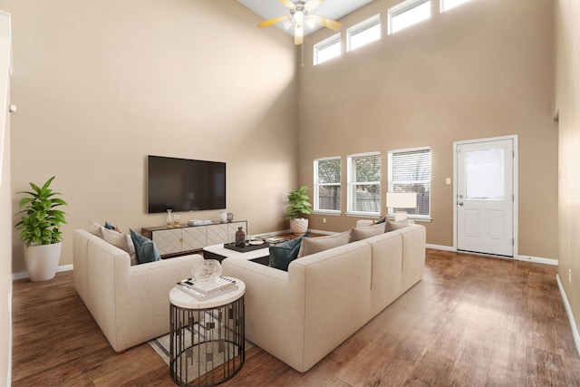 living area featuring a towering ceiling, ceiling fan, baseboards, and wood finished floors