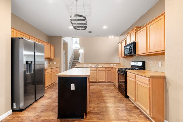 kitchen with pendant lighting, light brown cabinets, black appliances, light wood-type flooring, and a kitchen island