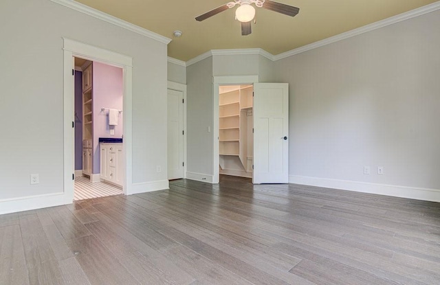 unfurnished bedroom with a walk in closet, ensuite bathroom, ornamental molding, ceiling fan, and hardwood / wood-style flooring