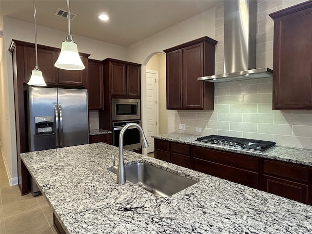 kitchen with sink, wall chimney exhaust hood, decorative backsplash, light stone counters, and stainless steel appliances