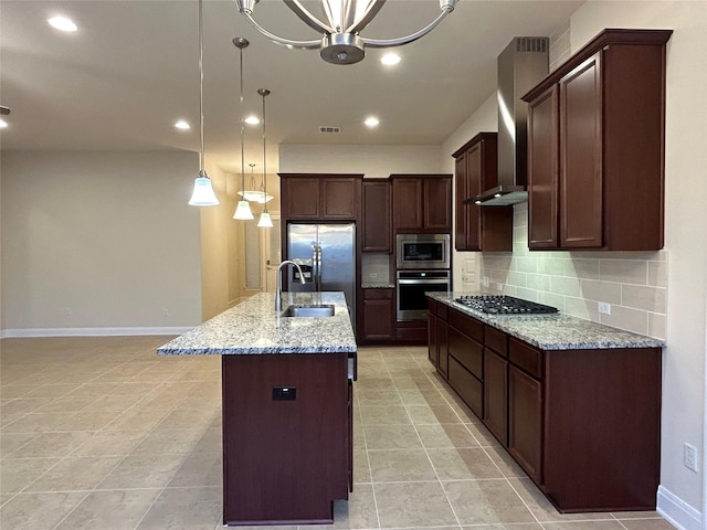 kitchen featuring light stone countertops, stainless steel appliances, wall chimney range hood, an island with sink, and pendant lighting