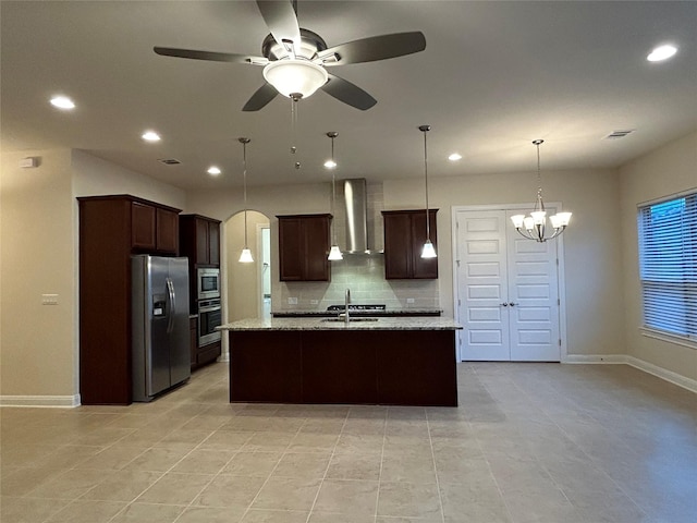 kitchen with a kitchen island with sink, wall chimney exhaust hood, decorative backsplash, light stone countertops, and stainless steel appliances