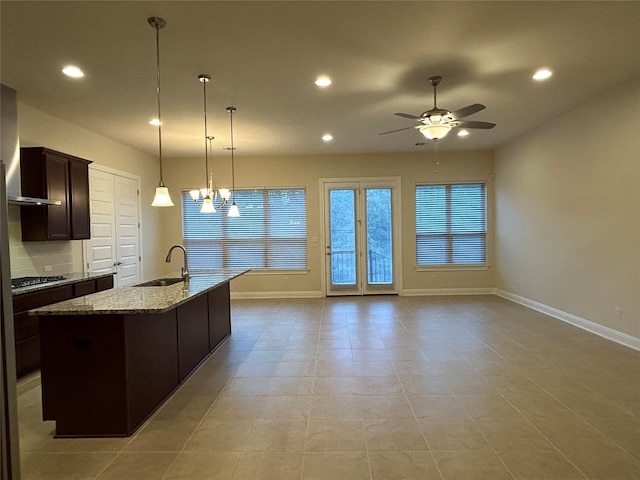 kitchen featuring a kitchen island with sink, ceiling fan with notable chandelier, hanging light fixtures, sink, and light stone countertops