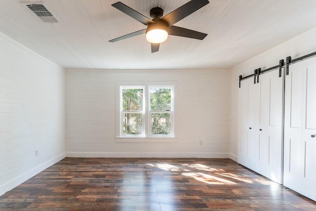 unfurnished bedroom featuring ceiling fan, a barn door, dark hardwood / wood-style floors, and a closet