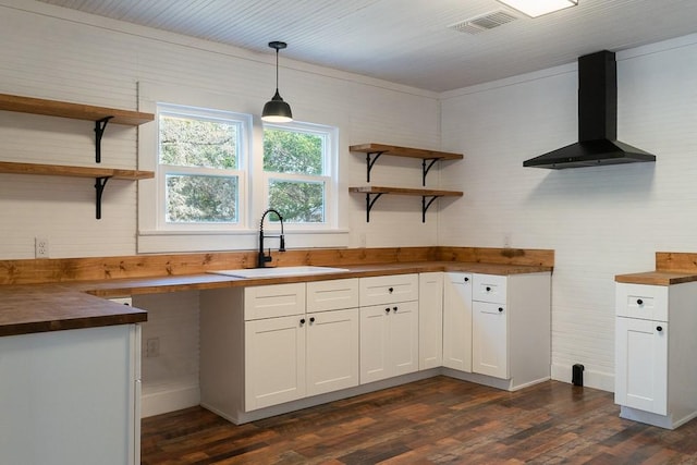 kitchen with white cabinets, butcher block countertops, hanging light fixtures, and wall chimney range hood