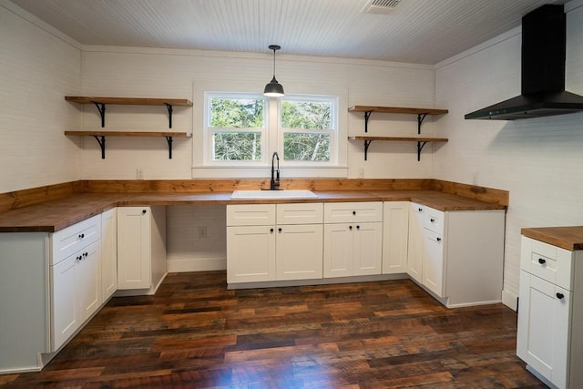 kitchen with wood counters, wall chimney exhaust hood, sink, decorative light fixtures, and white cabinetry