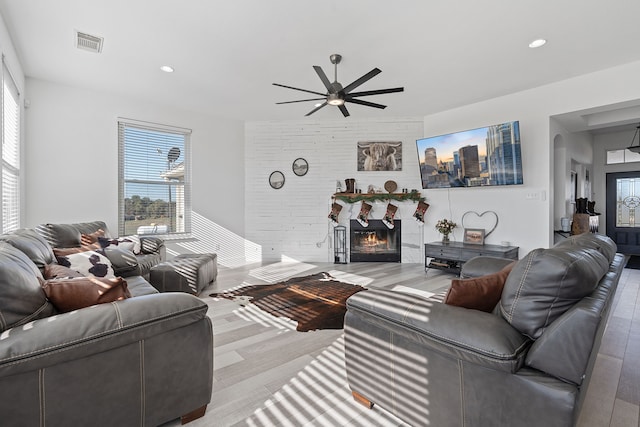 living room featuring arched walkways, recessed lighting, visible vents, a ceiling fan, and a warm lit fireplace