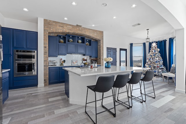 kitchen featuring double oven, light stone counters, a breakfast bar area, a center island, and open shelves