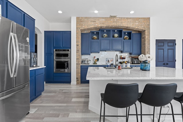 kitchen featuring stainless steel appliances, light stone countertops, an island with sink, and open shelves