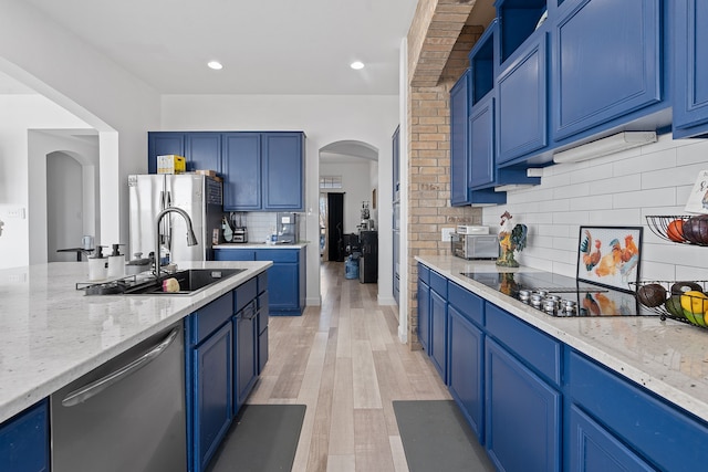 kitchen featuring light stone counters, arched walkways, appliances with stainless steel finishes, a sink, and blue cabinets