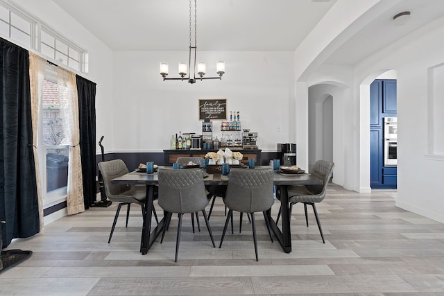 dining space with arched walkways, visible vents, a notable chandelier, and light wood-style flooring