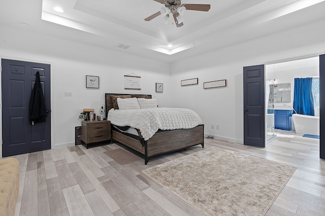 bedroom featuring a tray ceiling, baseboards, visible vents, and light wood finished floors