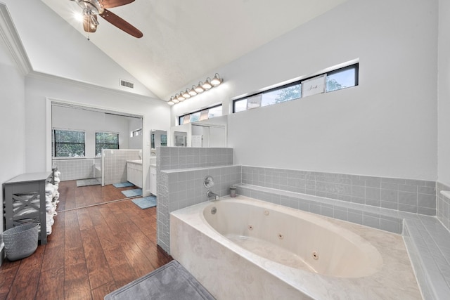 bathroom with lofted ceiling, wood-type flooring, vanity, tiled tub, and ceiling fan