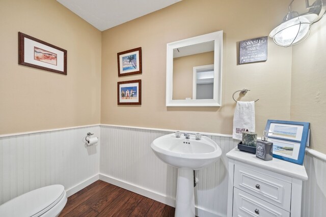 bathroom with wood finished floors, toilet, and a wainscoted wall