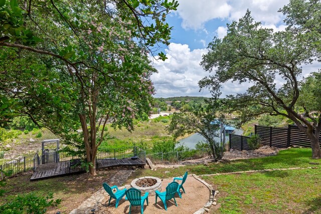 view of yard featuring a deck with water view, fence, and an outdoor fire pit